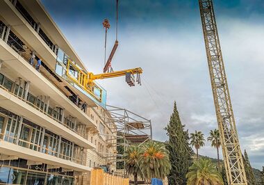 La méga-dalle est hissée jusqu'à l'ouverture du bâtiment à l'aide d'un système de ventouses à vide et d'une traverse à contrepoids