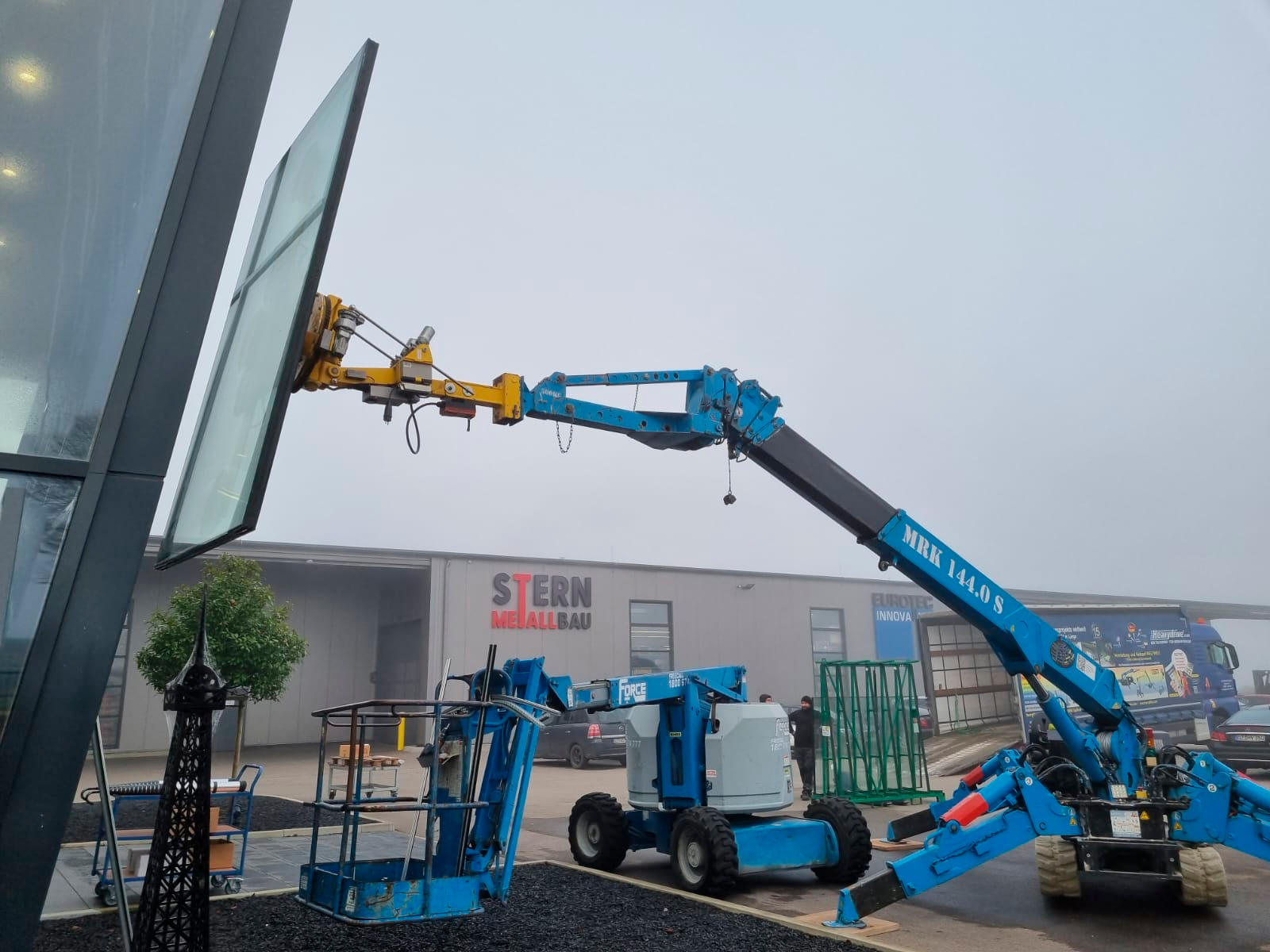 Remplacement d'une vitre de 220 kg (485 lb) sur une façade inclinée avec une grue MRK 144.0 S et un système à ventouses 450 K de Heavydrive